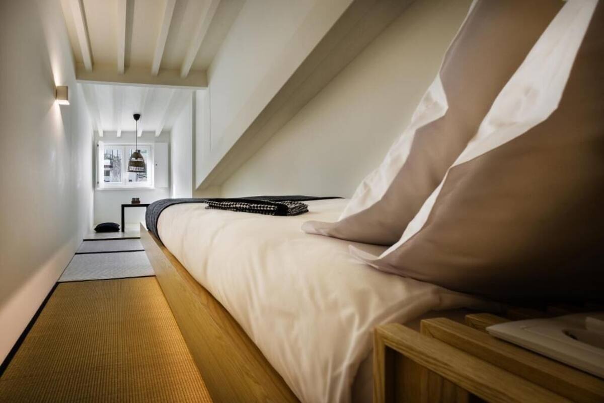 A bedroom with a bed, bedside table, and a view of the outside.