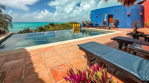 A pool area with a view of the ocean, outdoor seating, and a building with a blue exterior.