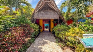 A thatched-roof structure with a paved pathway leading to it, surrounded by lush tropical vegetation.