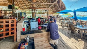 A beachside bar with wooden furniture, a thatched roof, and a view of the ocean.