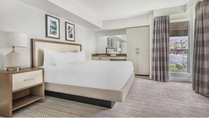 Ett hotellrum med en säng, ett nattduksbord, en byrå, ett badrum med en spegel och utsikt över omgivningarna.
