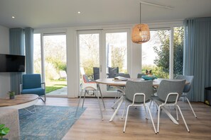 A modern living room with a dining area, large windows, and a flat-screen TV. - Luxury, Peace and Space for the Whole Family (De Koog)