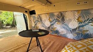 A compact interior with a foldable table, a patterned wall, and a bed with geometric pillows. - Fully equipped car to discover the whole island with ease (Les Abymes)