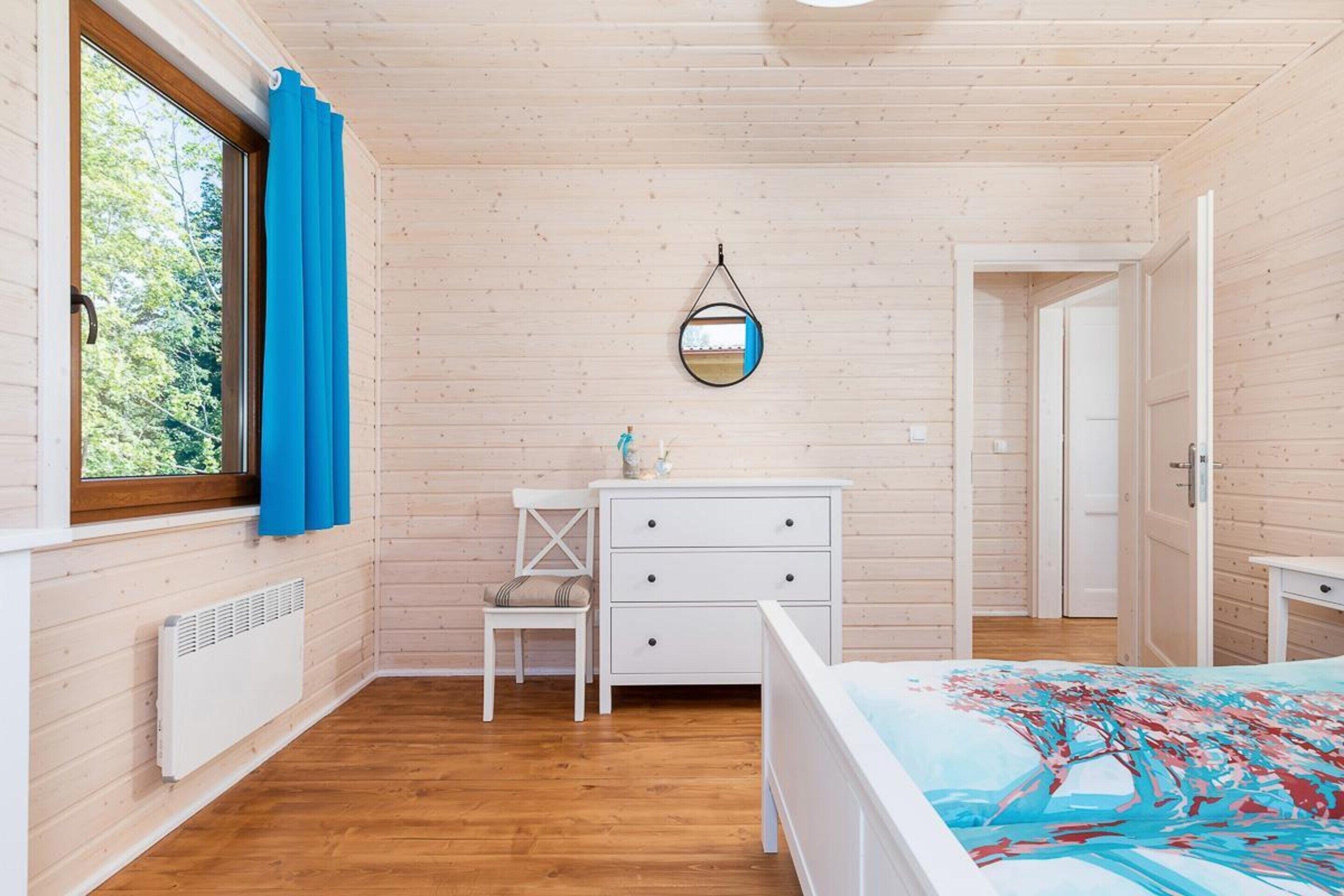 A wooden-paneled room with a bed, a white dresser, a chair, a mirror, and a radiator.