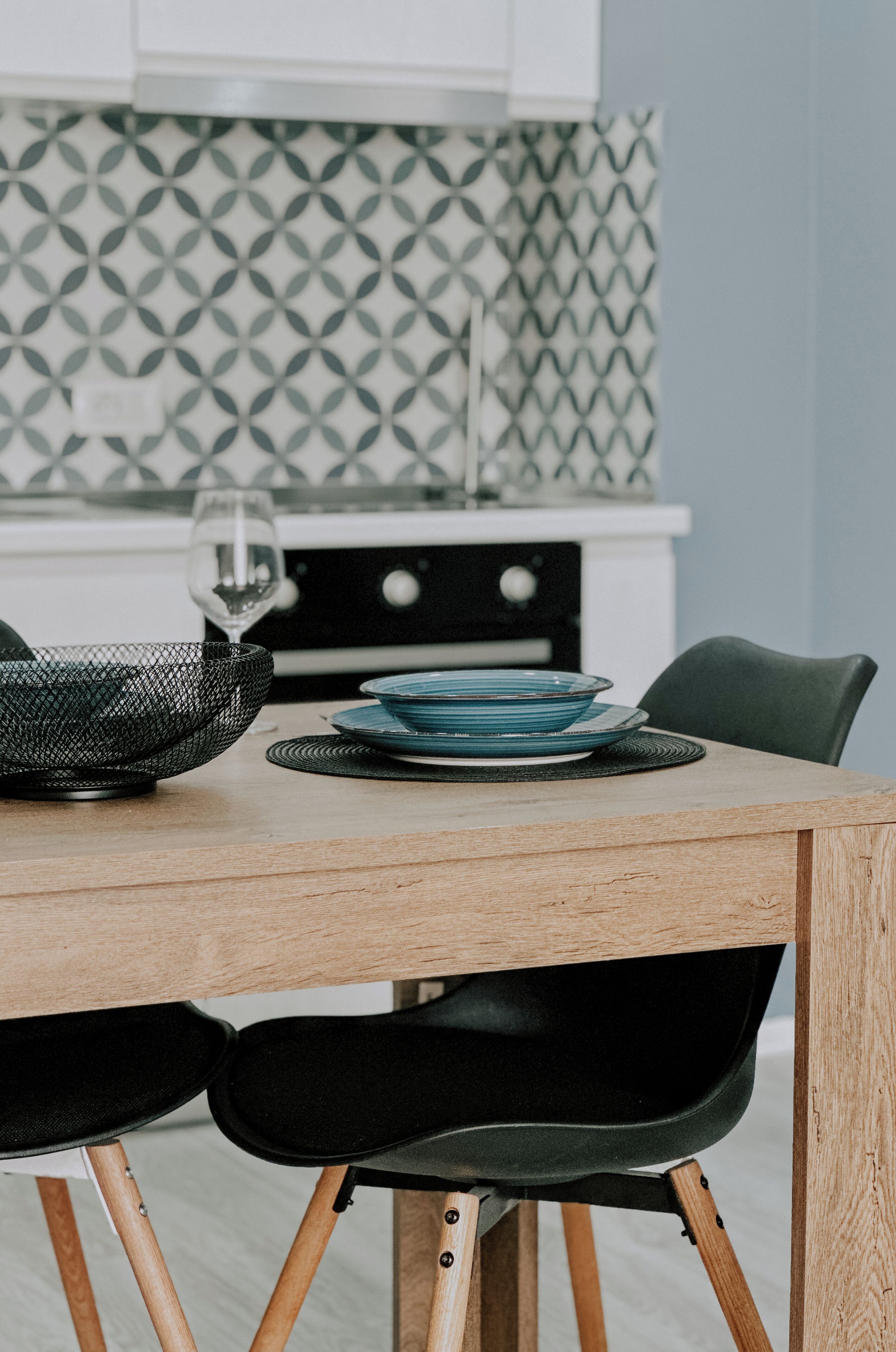 A dining table with a black mesh bowl, blue plates, and black chairs.