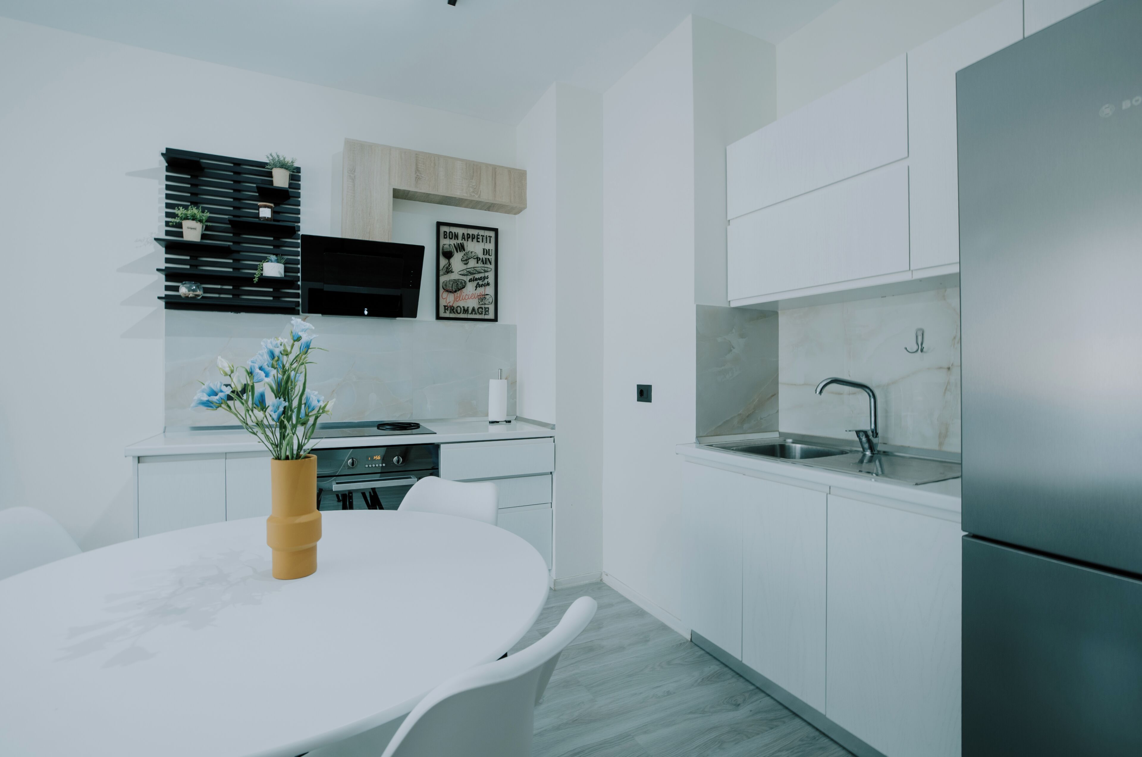 A modern kitchen with white cabinetry, a built-in oven, and a stainless steel refrigerator.
