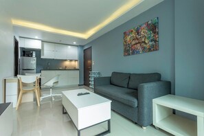 Ein modernes Wohnzimmer mit grauem Sofa, weißem Couchtisch und einer Küchenzeile mit weißen Schränken und einer Mikrowelle.