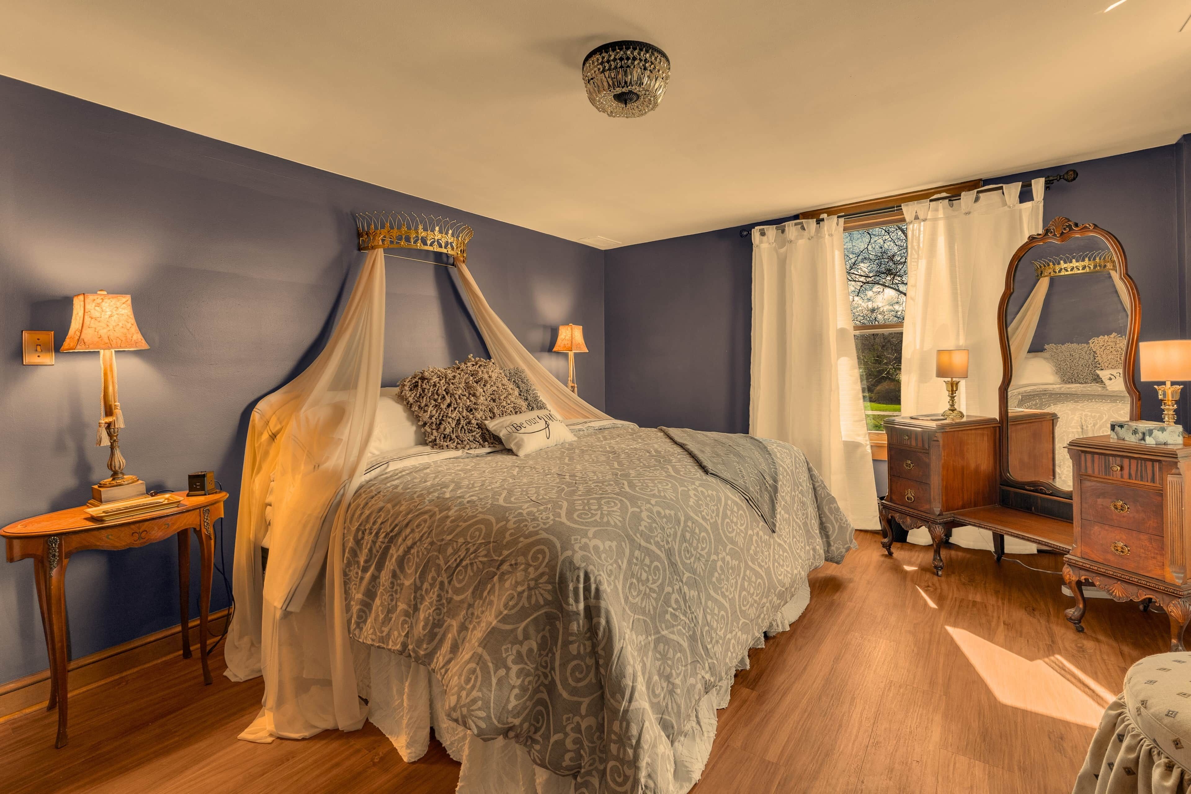 Une chambre à coucher avec un lit à baldaquin, une commode en bois, un miroir et une table de chevet avec des lampes.