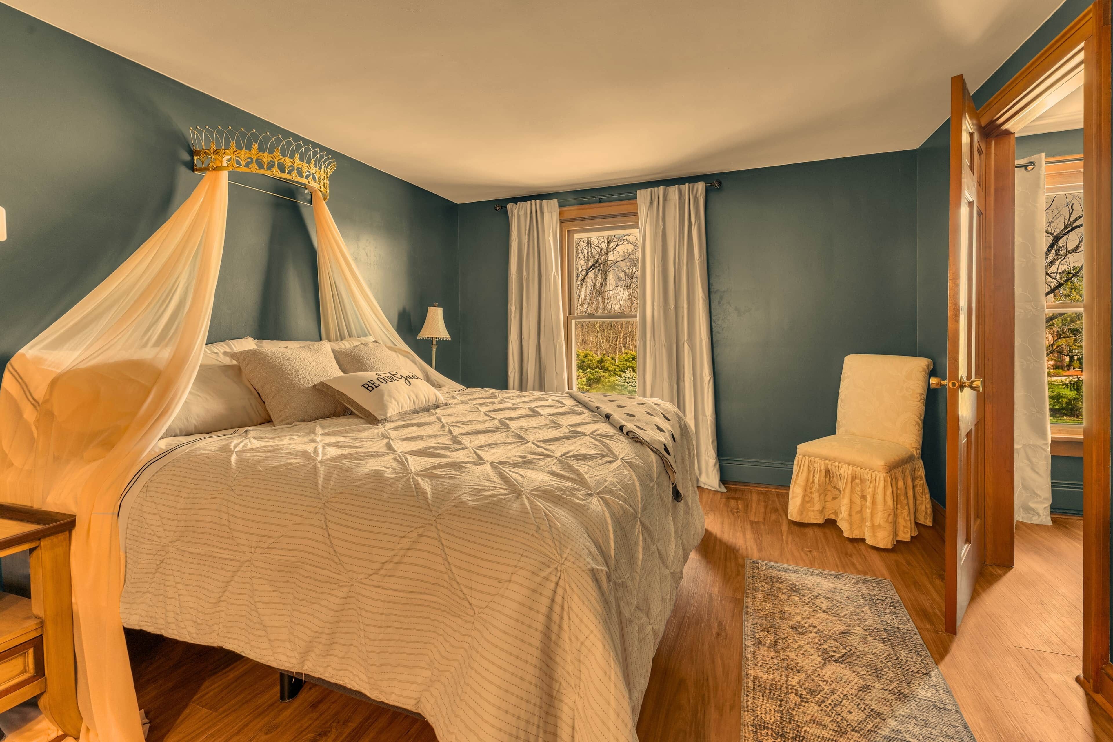 A bedroom with a canopy bed, a chair, a window with curtains, and a rug.