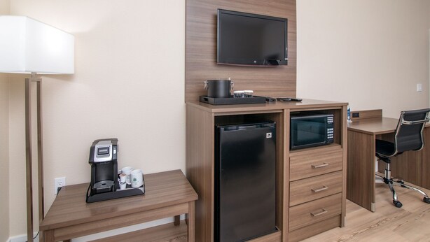 A compact hotel room with a kitchenette, a flat-screen TV, a refrigerator, a microwave, a coffee maker, and a desk with a chair. - King Bed Suite in a Hotel (Pollock Pines)