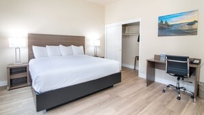 A modern hotel room with a large bed, bedside lamps, a desk with a chair, and a painting on the wall. - King Bed Suite in a Hotel (Pollock Pines)