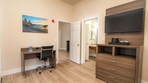 A hotel room with a wooden desk, a chair, a television, and a painting on the wall. - King Bed Suite in a Hotel (Pollock Pines)
