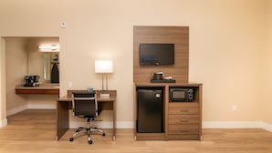 A hotel room with a wooden desk, a chair, a flat-screen TV, a mini-fridge, a microwave, and a coffee maker.