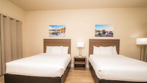 A hotel room with two beds, wooden headboards, a nightstand with a lamp, and two wall-mounted paintings.