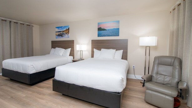 A hotel room with two beds, a chair, a lamp, and two paintings on the wall. - 2 Queen Bed Room- Handicap (Pollock Pines)