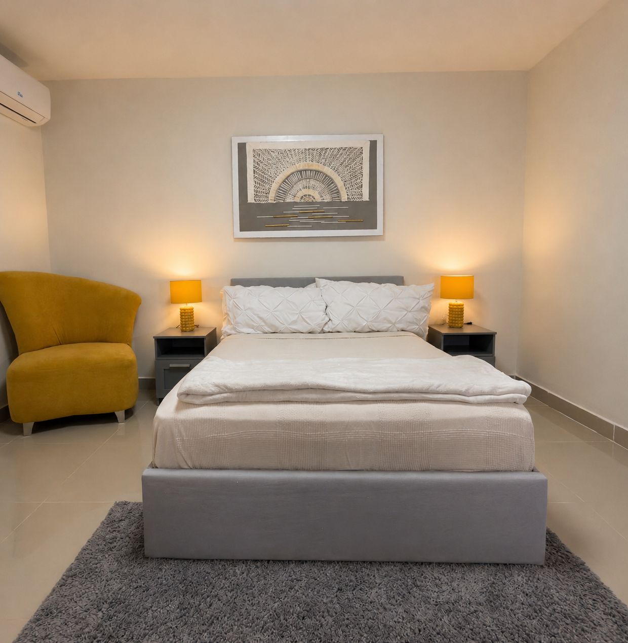 A modern bedroom with a bed, two bedside lamps, a chair, and a wall-mounted artwork.