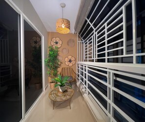A narrow corridor with a rattan table, potted plants, and a wicker chair. - SAN ISIDRO URBAN SUITE (Santo Domingo Este)