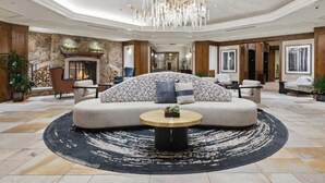 A spacious lobby with a large sofa, a round coffee table, a chandelier, and a fireplace.