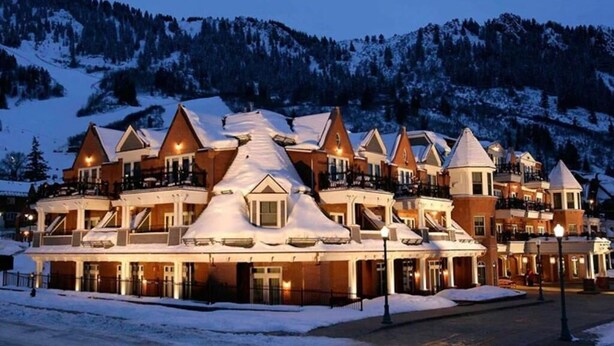 A multi-story hotel with a snow-covered roof, multiple balconies, and a mountainous backdrop.