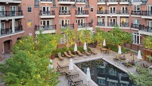 A multi-story building with a courtyard featuring outdoor seating, a swimming pool, and greenery.