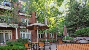 A patio with outdoor seating, a brick building, and surrounding greenery.