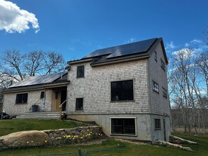 A two-story house with a sloped roof, a stone retaining wall, and a garden with daffodils.