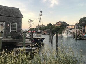 A marina with boats docked, wooden buildings, and a crane in the background.