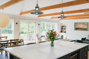 A spacious kitchen with a large island, wooden beams, pendant lights, and a view of the outdoors.