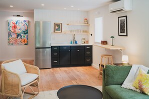 A modern kitchen with a stainless steel refrigerator, black cabinets, and a wooden countertop. There is a wicker chair and a green sofa with a throw pillow.