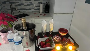 Eine Küchenarbeitsplatte mit einer Champagnerflasche, Wasserflaschen, einer Schale Erdbeeren, einer Kerze und einer Blumenkomposition.