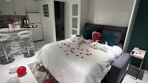 Ein modernes Hotelzimmer mit einem großen Bett, einer kleinen Küchenzeile und einer Sitzecke mit Hocker.