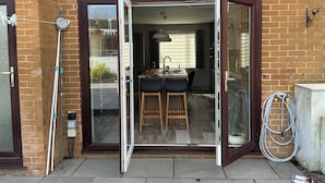 A residential property with a sliding glass door entrance, a small kitchen with a sink and stools, and a garden hose on the right. - Take a Break. Cozy Double Room. Very modern home. Full use of Bathroom,Kitchen (Leyland)