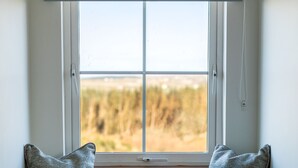 A window seat with two pillows, a white door below, and a view of a natural landscape. - Peaceful family hideaway near Doolin with Aran views & stunning sunsets. (Doolin)