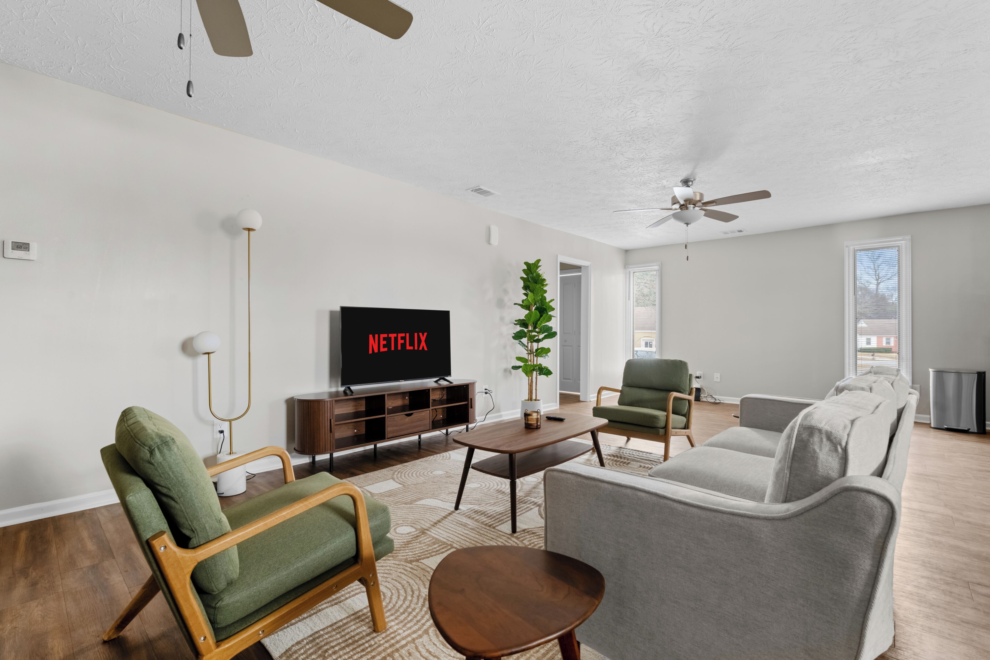 A modern living room with a flat-screen TV, a ceiling fan, and a large window.