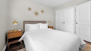 Un dormitorio ordenado con cama, dos mesitas de noche con lámparas, armario y decoración en la pared.