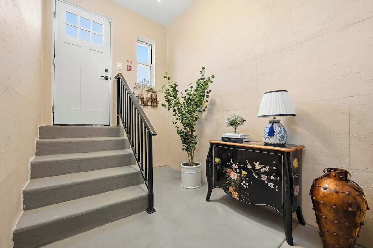 A staircase with a white door at the top, a potted plant, a console table with a vase, and a decorative vase.