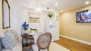 A dining area with a table, chairs, a chandelier, a refrigerator, and a television on the wall.