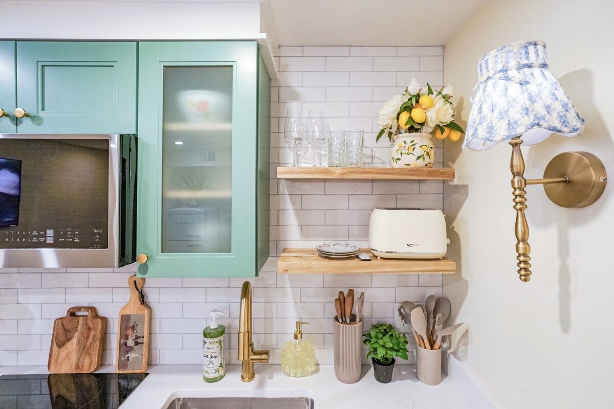 A kitchen with teal cabinets, a microwave, a toaster, a sink, and a wall-mounted lamp.