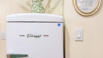 A white refrigerator with the brand name 'Classic' on it, placed against a wall with a framed quote and a potted plant.