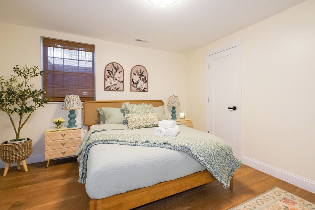 A bedroom with a bed, bedside tables, a lamp, a potted plant, and artwork on the wall.