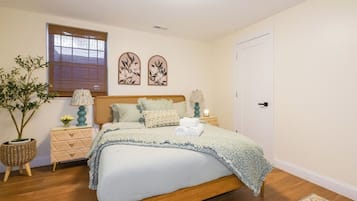 A bedroom with a bed, bedside tables, a lamp, a potted plant, and artwork on the wall.