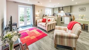 A modern living room with a sofa, armchair, and a dining area with a table and chairs. - Cosy countryside lodge in quiet surroundings - Pass the Keys (Shrewsbury)