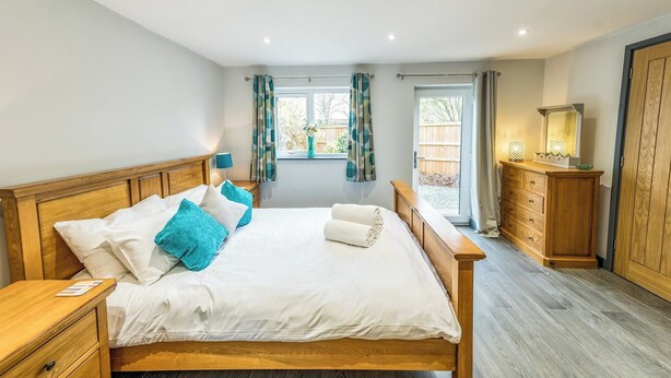 A bedroom with a wooden bed, a nightstand, a dresser, and a window with curtains. - Cosy countryside lodge in quiet surroundings - Pass the Keys (Shrewsbury)