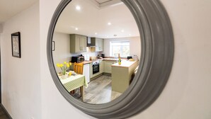 A round mirror reflecting a kitchen with a dining table, a window, and a view of the outdoors. - Cosy countryside lodge in quiet surroundings - Pass the Keys (Shrewsbury)