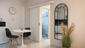 Une cuisine moderne équipée d’un four à micro-ondes, d’une table de salle à manger ronde avec deux chaises, d’un grand miroir et d’une plante en pot.