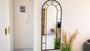 Une chambre d’hôtel avec un grand miroir en arc de cercle, un lit, une petite plante et un canapé gris.