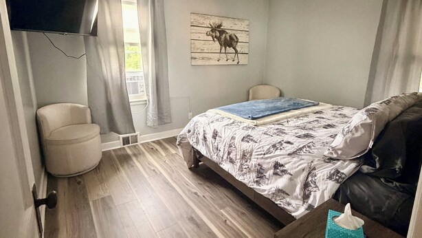 Een slaapkamer met een bed, een stoel, een nachtkastje, een wandtelevisie en een plafondventilator.