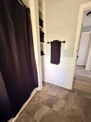 Een badkamer met een douchegordijn, een handdoekrek met een handdoek en een betegelde vloer.