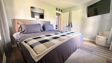 Ein Schlafzimmer mit einem Bett, einem an der Wand befestigten Fernseher und einer Tür zu einem anderen Raum.