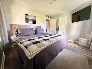 A bedroom with a bed, a television mounted on the wall, and a door leading to another room. - Spacious Country Retreat – Perfect for Families, Groups & Getaways (Plattsburgh)